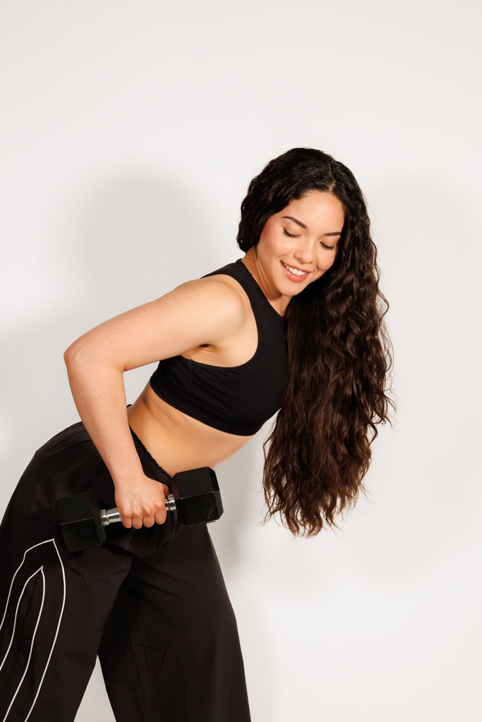 Coach is posing wearing aablack workout outfit and holding dumbells.